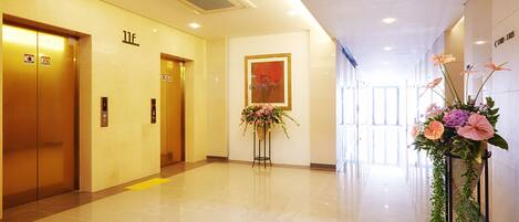 Un moderno vestíbulo de hotel con dos ascensores, un mostrador de recepción y un gran arreglo floral.