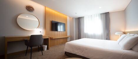 Habitación de hotel con cama, escritorio con silla, televisor montado en la pared y un amplio ventanal con cortinas.