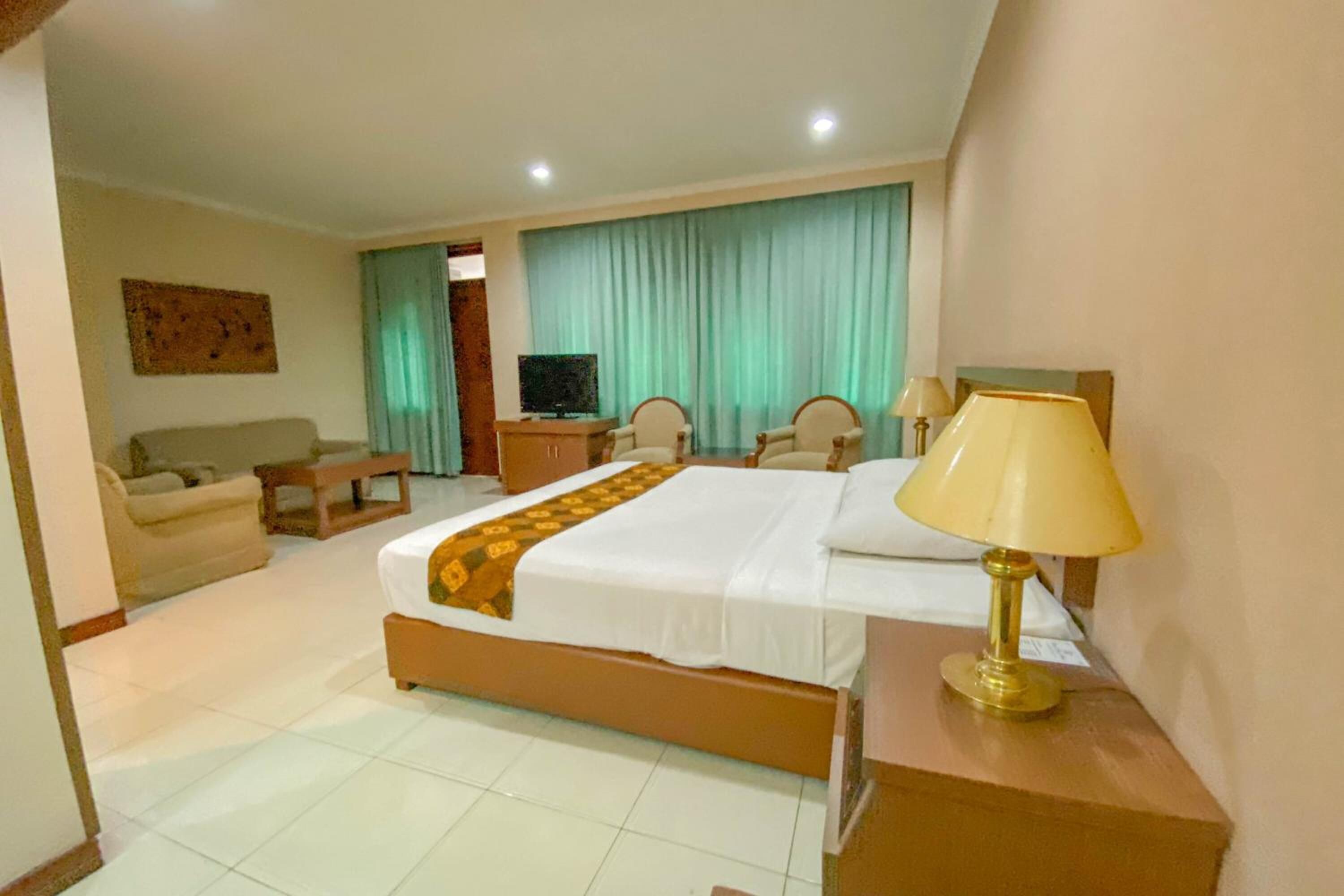 A hotel room with a bed, a desk, a chair, a television, and a lamp.