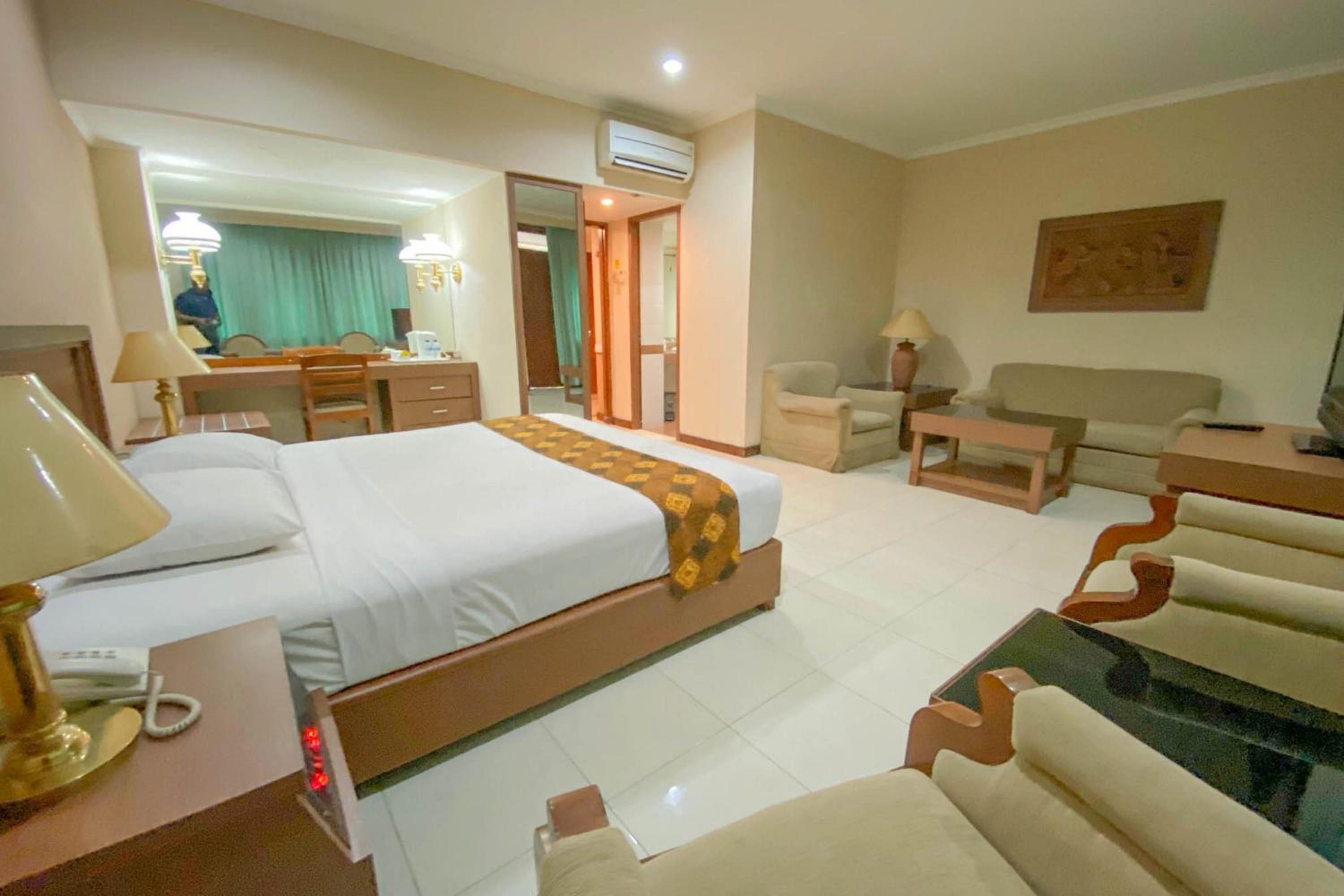 A hotel room with a bed, a desk, a chair, a sofa, and a television.