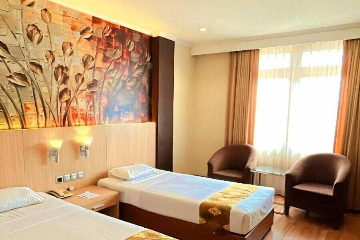 A hotel room with two beds, a desk, a chair, and a large wall mural.