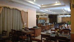 Een restaurant met meerdere eettafels en stoelen, een bar en een zichtbare keuken op de achtergrond.
