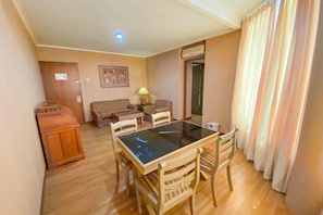 A compact living space with a dining table, chairs, a sofa, a lamp, and a door leading to another room. - Riyadi Palace Hotel (Surakarta)