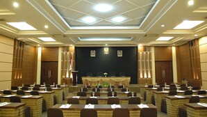 Een vergaderruimte met een hoge plafond, inbouwverlichting en een podium met spreekgestoelte.