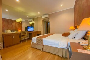 A hotel room with a bed, desk, TV, and a lamp. - Riyadi Palace Hotel (Surakarta)