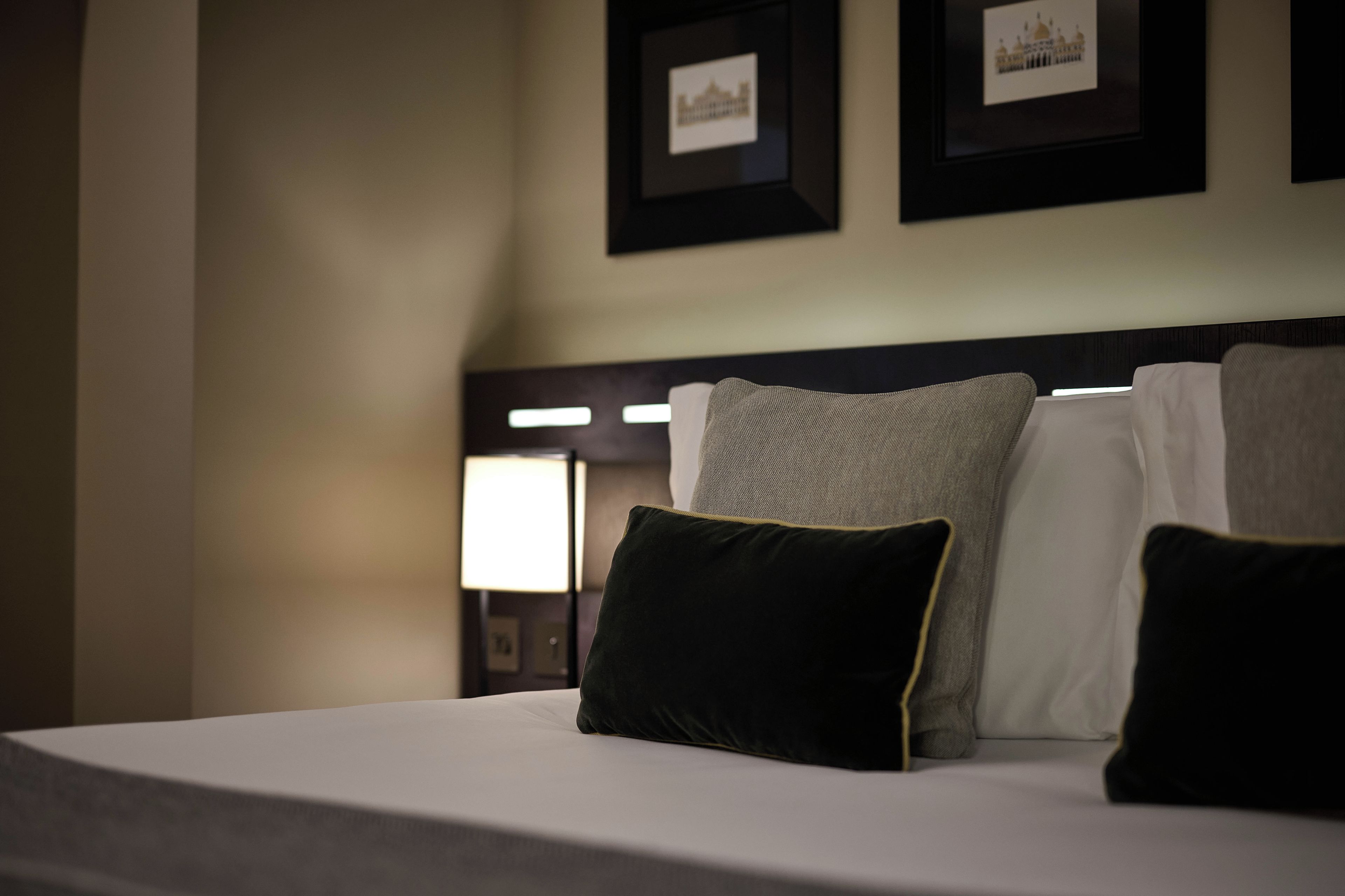 Een hotelkamer met een net opgemaakt bed, een hoofdbord met een lamp en ingelijste foto's aan de muur.
