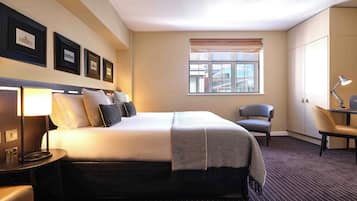 A hotel room with a bed, a desk, a chair, a lamp, and a window with a city view.