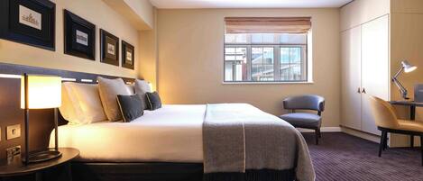 A hotel room with a bed, a desk, a chair, a lamp, and a window with a city view.