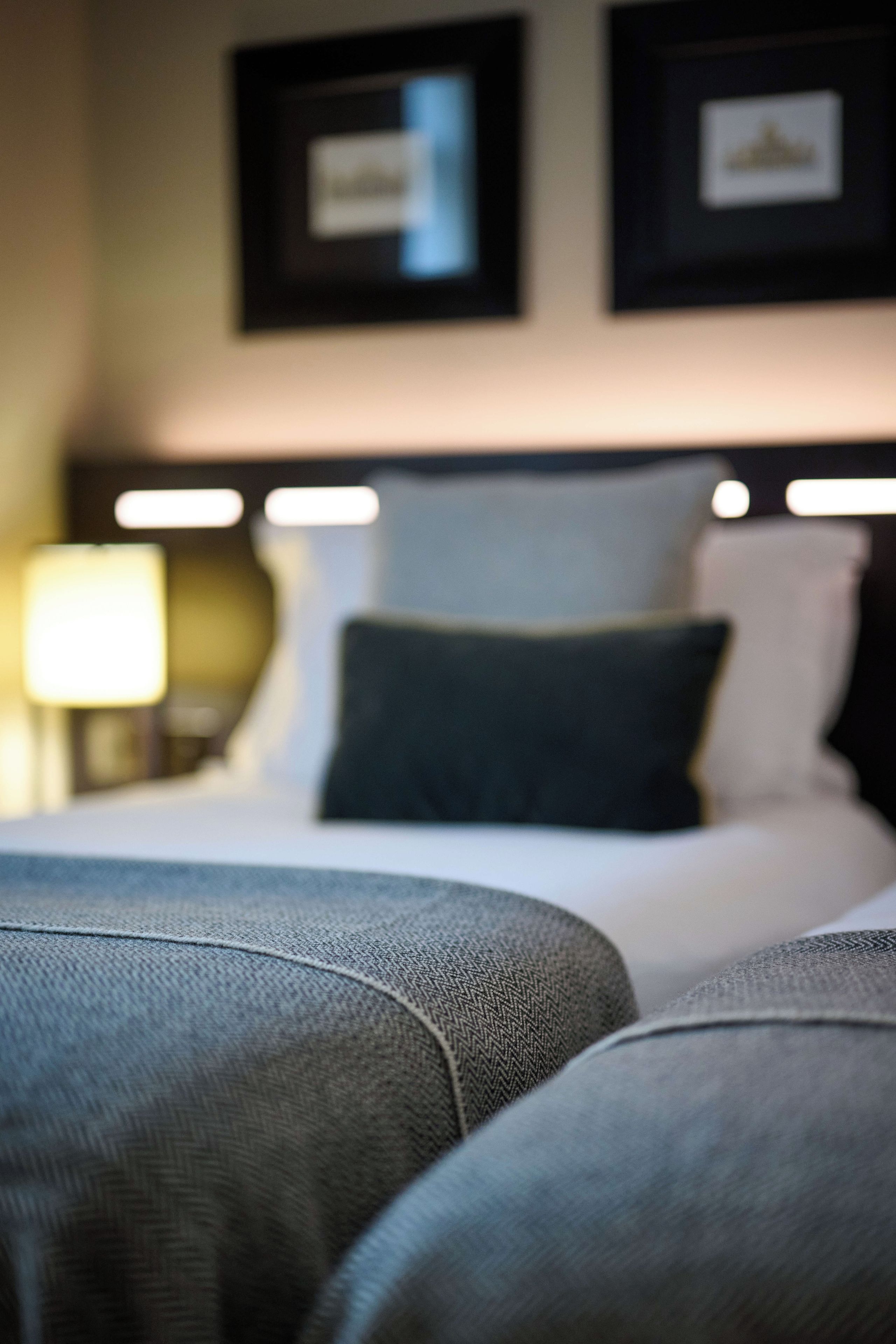 Habitación de hotel con cama bien hecha, cabecera con iluminación integrada y un cuadro colgado en la pared.