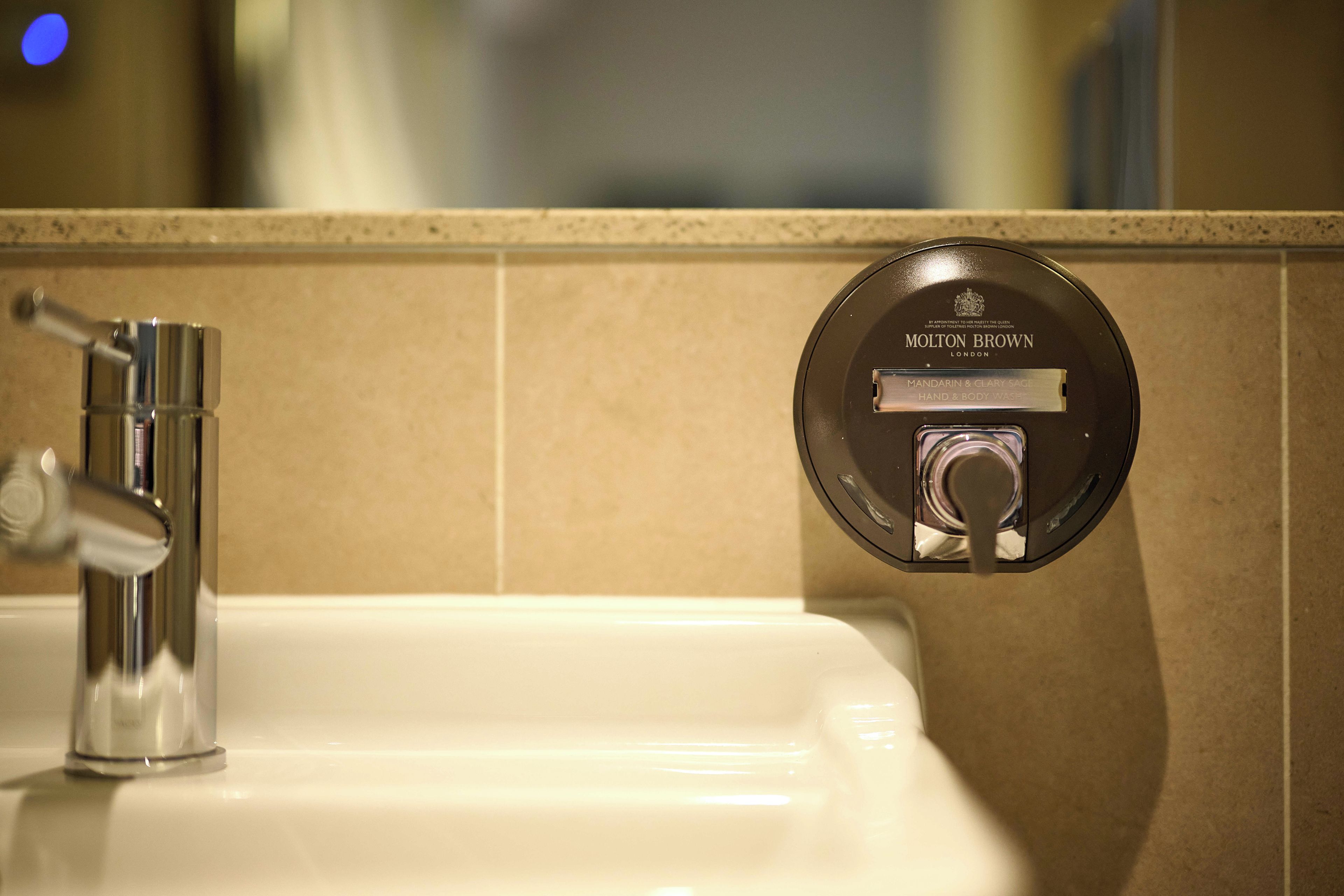 A bathroom sink with a modern faucet and a wall-mounted hand and body wash dispenser.
