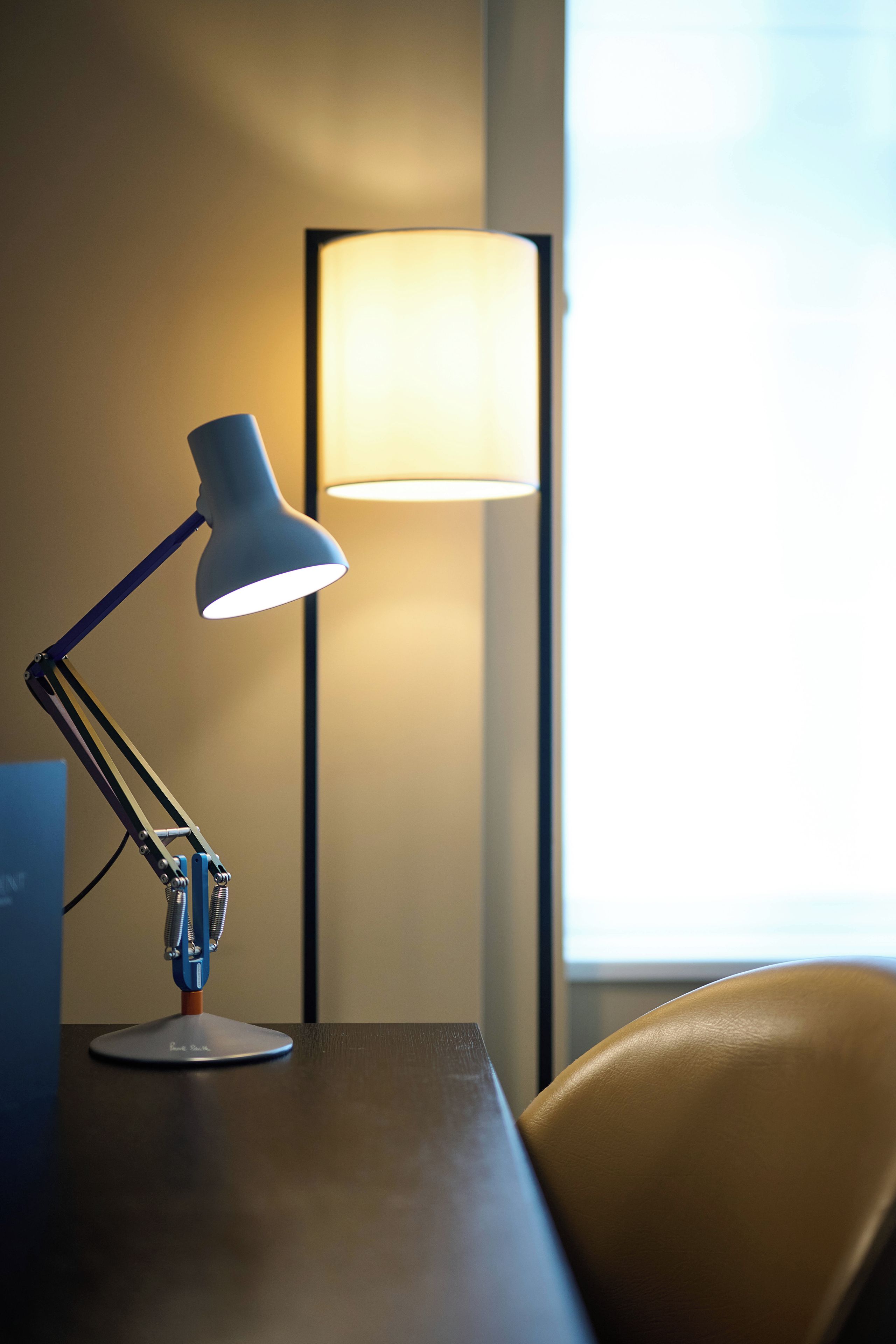 A desk with a desk lamp and a lamp in the background.
