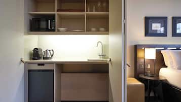 Une chambre d’hôtel compacte comprenant un coin cuisine, un lit, une table de chevet avec une lampe et un petit coin salon.