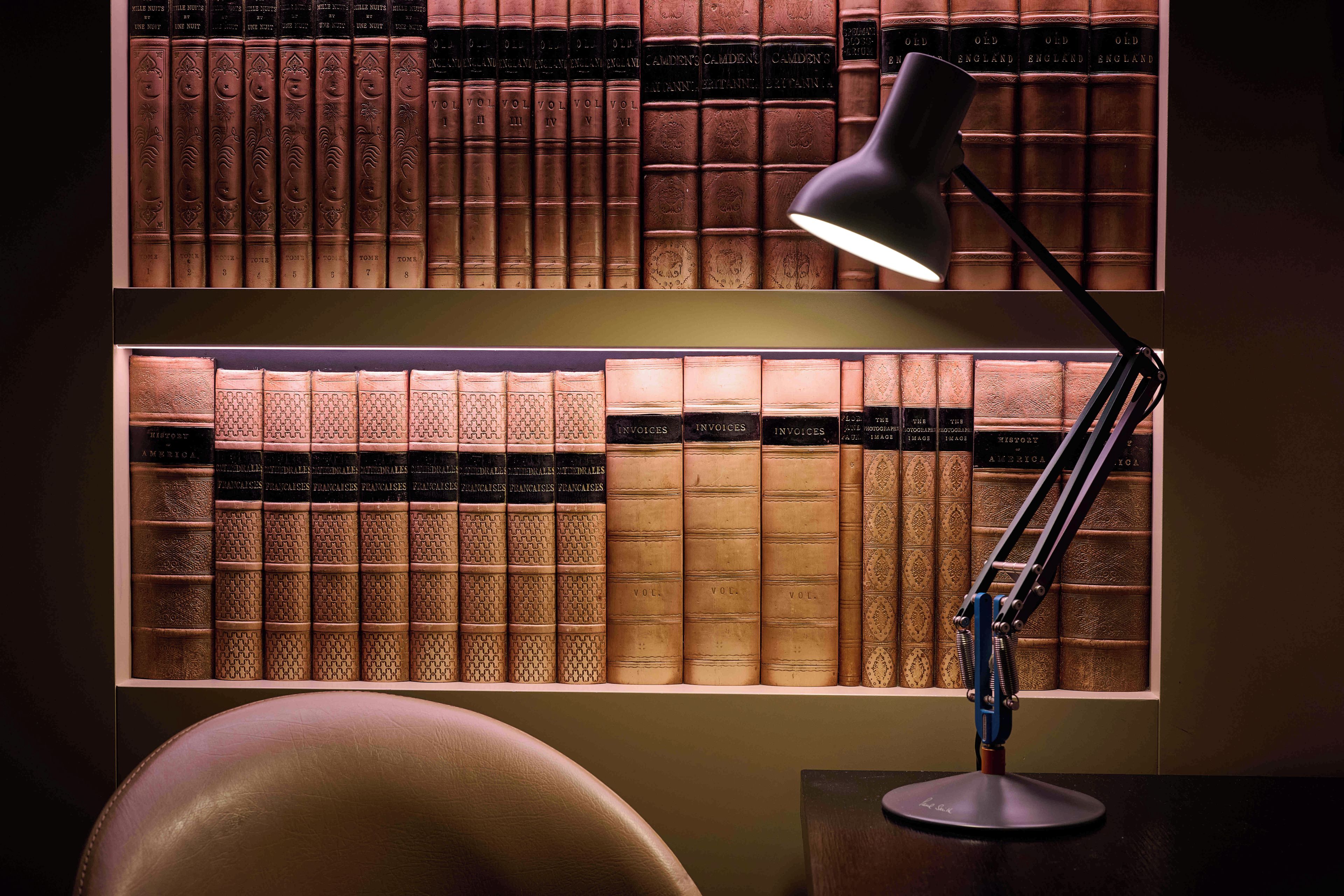 A desk with a lamp and a collection of bookshelves filled with books.