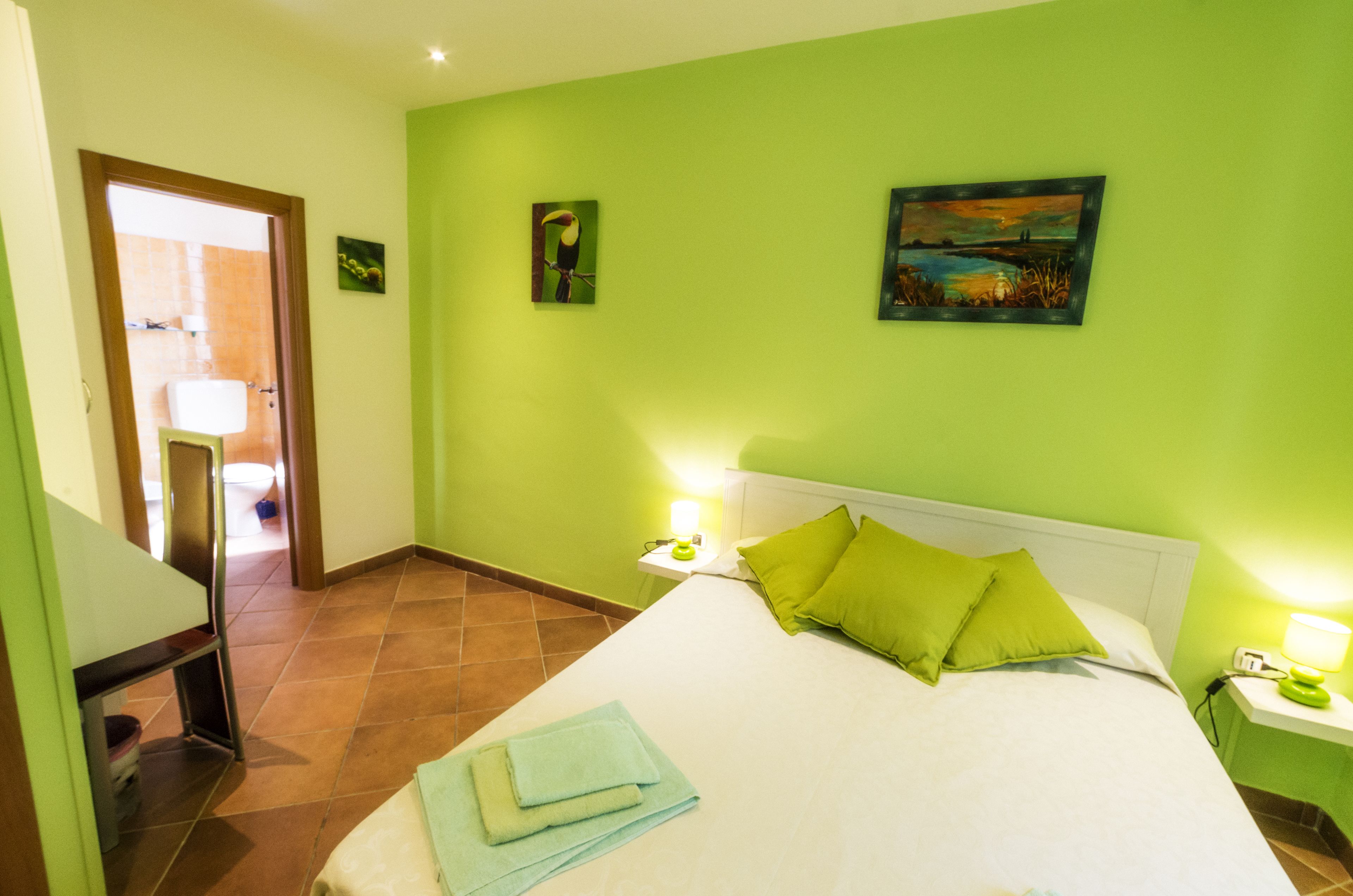 Une chambre d’hôtel avec un lit, des murs verts, un tableau et une table de chevet avec une lampe.