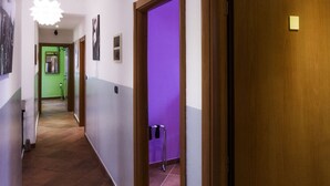 Un pasillo con piso de baldosas, puertas de madera y una habitación iluminada de púrpura al final.