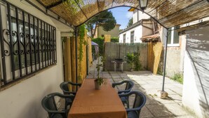 Un área de comedor al aire libre con techo, una mesa, sillas, una planta en maceta y una parrilla.