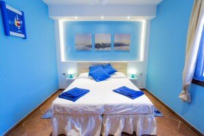 A double bed with white bedding and blue pillows, a nightstand with a lamp, and three wall-mounted paintings. - Hotel Rainbow (Taggia)