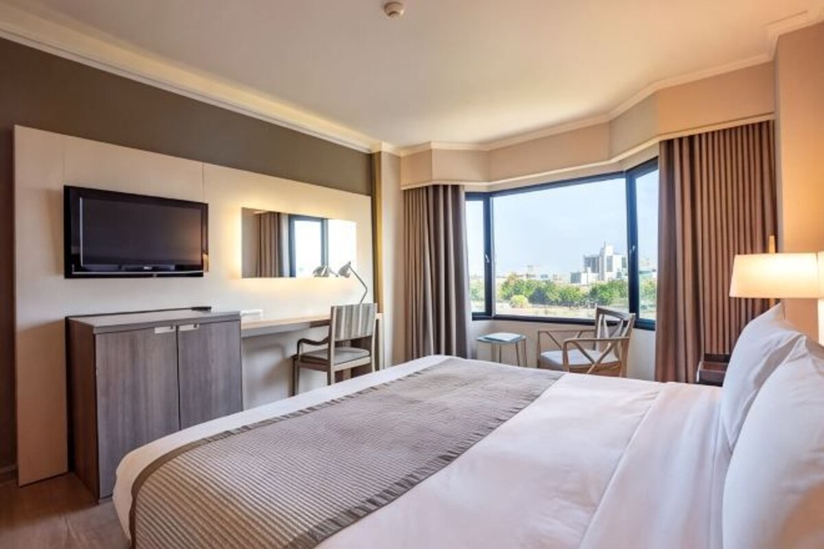 Une chambre d’hôtel avec un grand lit, un bureau, une télévision et une vue sur la ville.