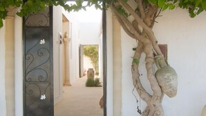 A covered entrance with a metal gate, a tree with hanging pots, and a pathway leading to a building. - Menzelcaja (Aghir)