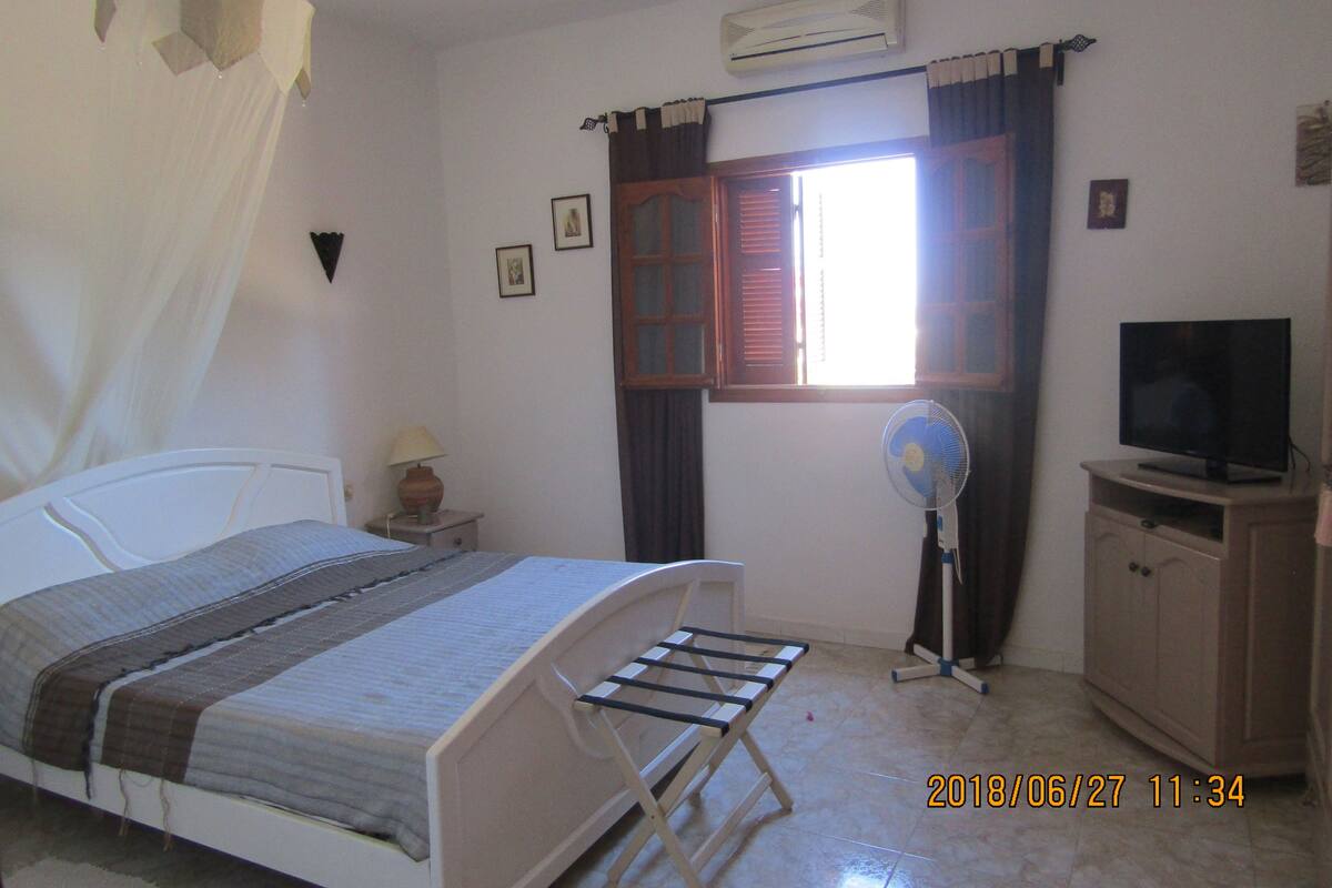 Une chambre à coucher avec un lit, une télévision, un ventilateur et une fenêtre avec des rideaux.