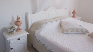 A neatly made bed with a white headboard and a decorative pillow. There is a bedside table with a lamp and a small box. - Menzelcaja (Aghir)