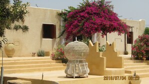 A building with a beige facade, a large decorative urn, and vibrant pink bougainvillea flowers. - Menzelcaja (Aghir)