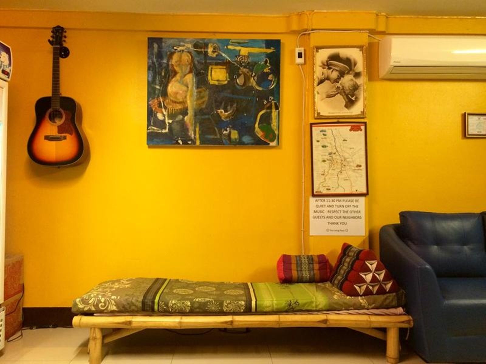 A room with a bed, a guitar, a map, and artwork on the walls.