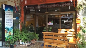 A guesthouse with a wooden bench outside, a signboard advertising activities and best trips, and a large window with a view of the interior. - The Living Place 2 - Hostel (Chiang Mai)