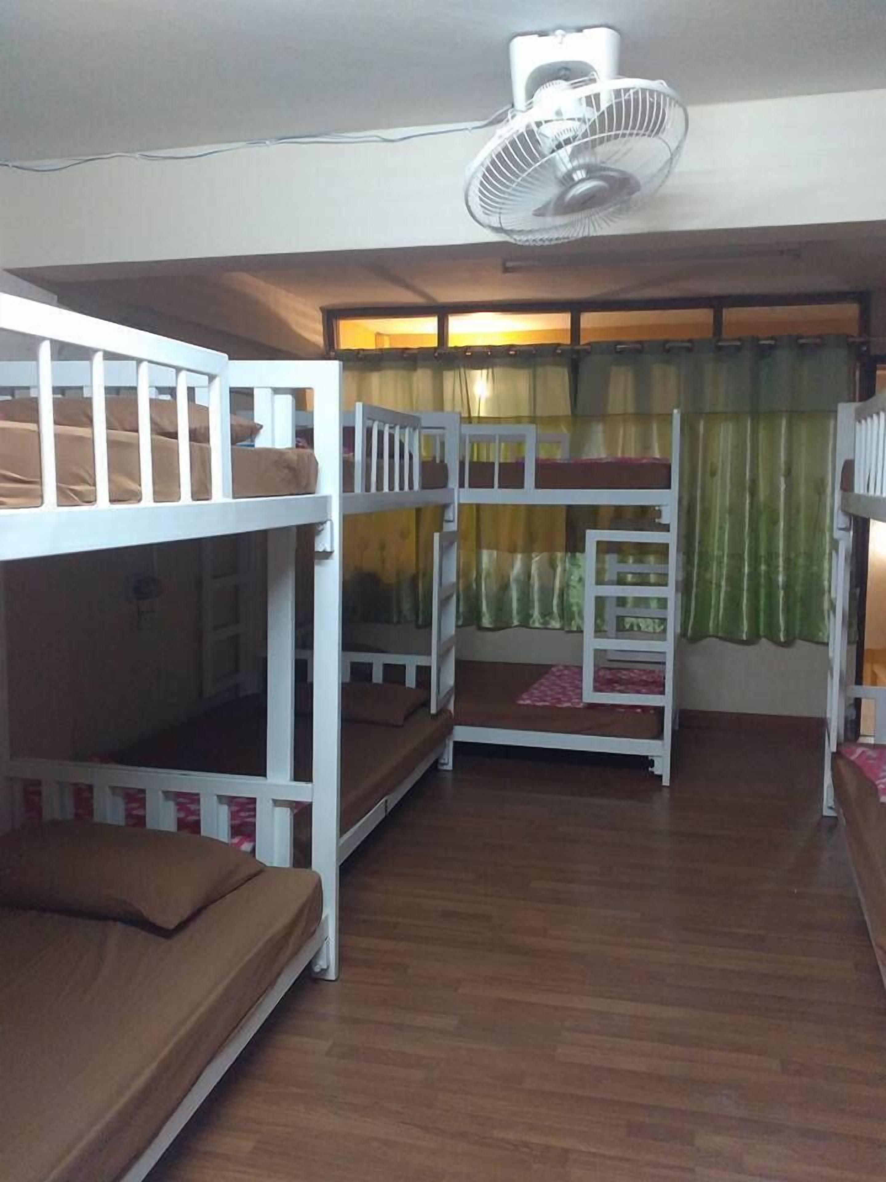 A room with bunk beds, a ceiling fan, and a window with curtains.