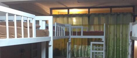 A room with bunk beds, a ceiling fan, and a window with curtains.