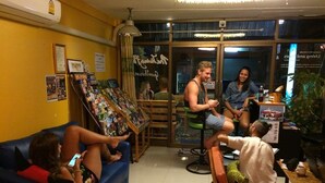 A cozy indoor space with a blue couch, a small table with a cup, and a chair with a colorful cushion. - The Living Place 2 - Hostel (Chiang Mai)