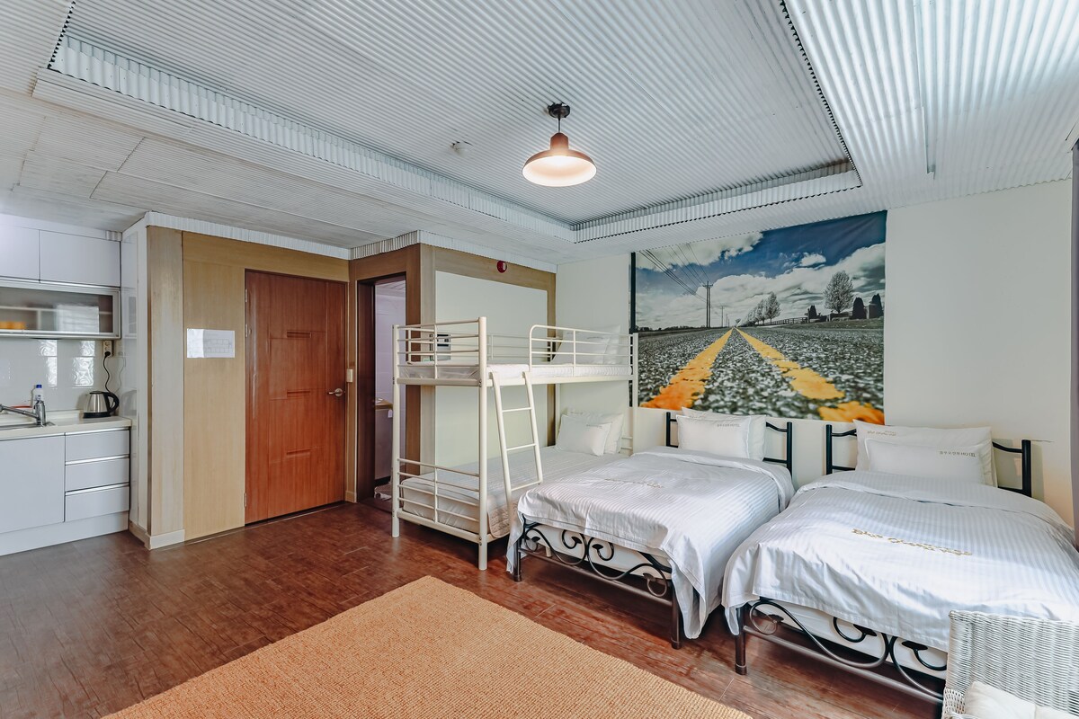 A room with bunk beds, a kitchenette, and a painting of a road.