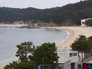 A coastal area with a beach, a rocky shoreline, and a building with signage. - Residence Hotel Blue Ocean View (Ulsan)
