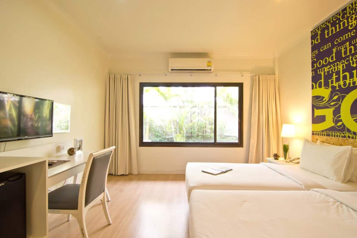 A hotel room with a bed, a desk with a chair, a television, and a window with curtains.