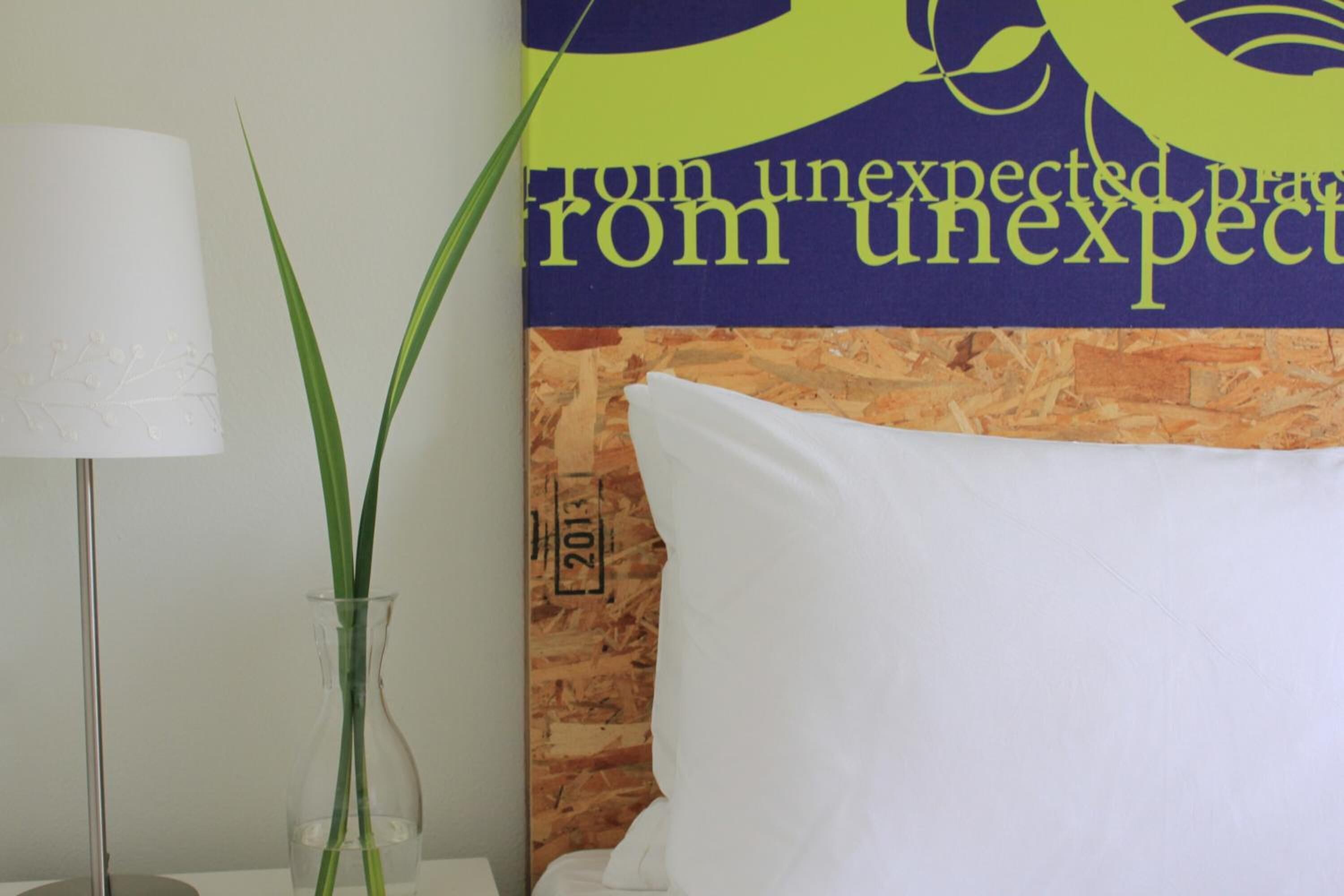 A room with a white pillow, a clear vase with green plants, and a wall with a poster.