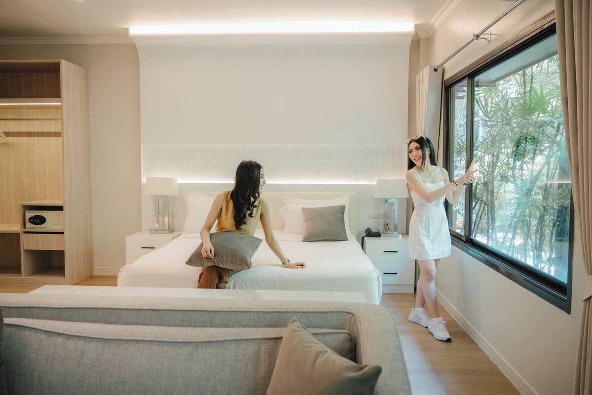 A modern hotel room with a large bed, bedside tables, a sofa, and a large window with a view of greenery.