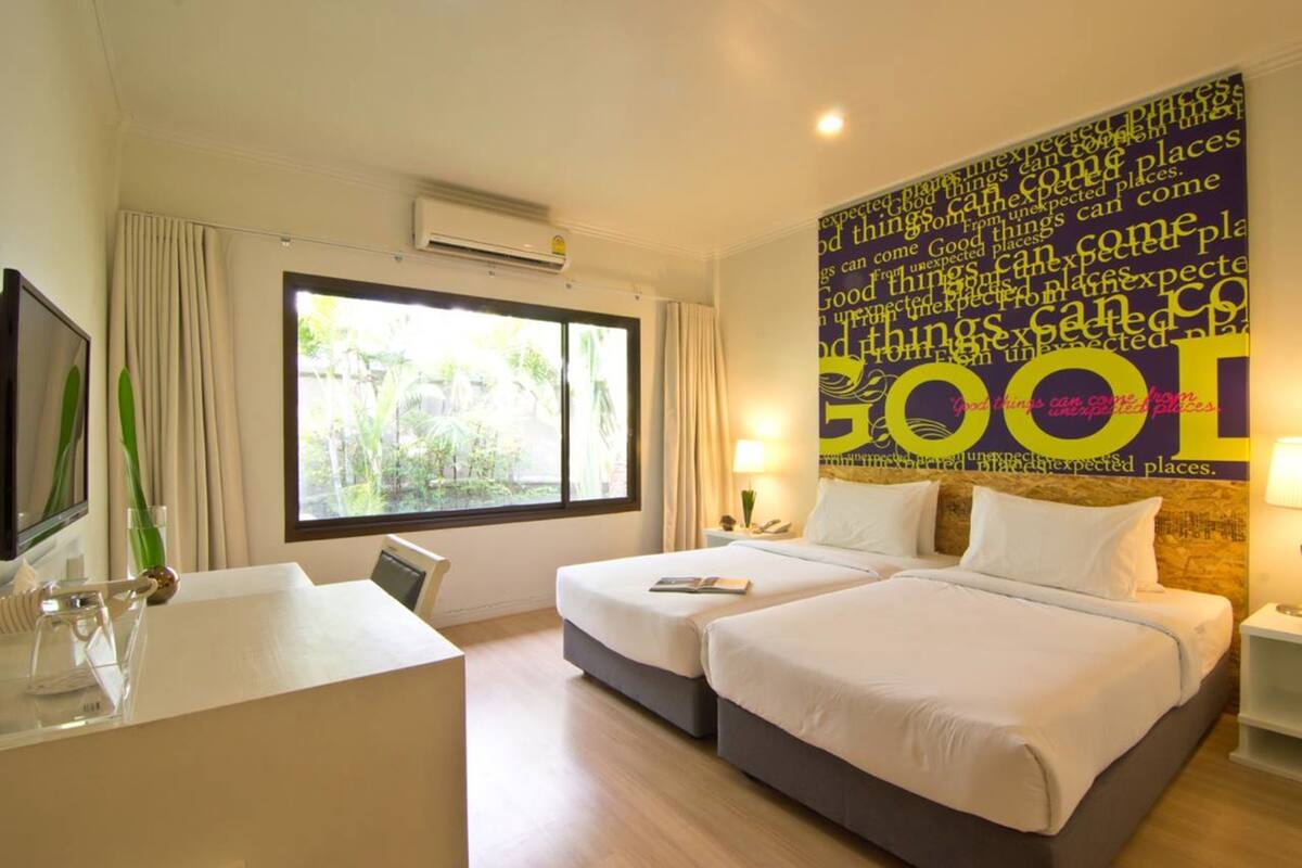 A hotel room with two beds, a desk, a TV, and a large window.