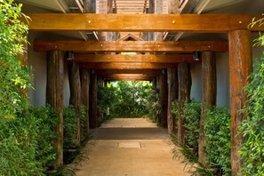 Un couloir aux poutres et colonnes en bois, bordé d’une végétation luxuriante.