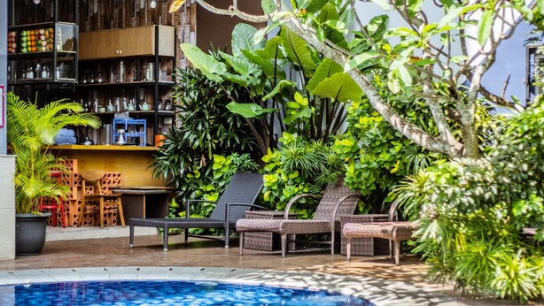 A poolside area with wicker chairs, a bar area with shelves, and lush greenery. - Tjokro Style Yogyakarta (Yogyakarta)
