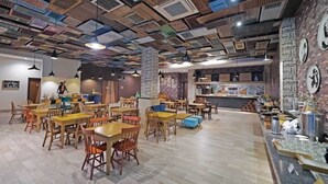 A spacious cafe with wooden tables and chairs, a brick wall with artwork, and a ceiling with exposed ductwork. - Tjokro Style Yogyakarta (Yogyakarta)
