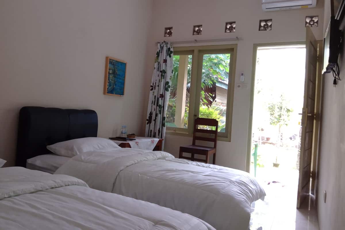 A hotel room with two beds, a painting on the wall, a window with curtains, and an air conditioning unit.