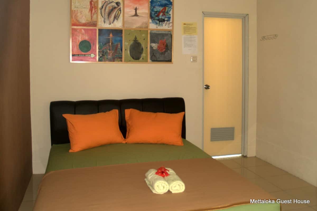 A hotel room with a bed, orange pillows, a green bedspread, and artwork on the wall.