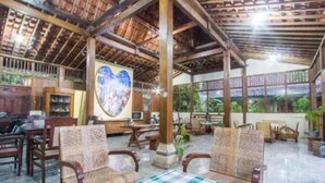 A spacious indoor area with wooden furniture, a checkered table, and a large heart-shaped artwork on the wall. - Mettaloka Guest House and Art Space (Borobudur)