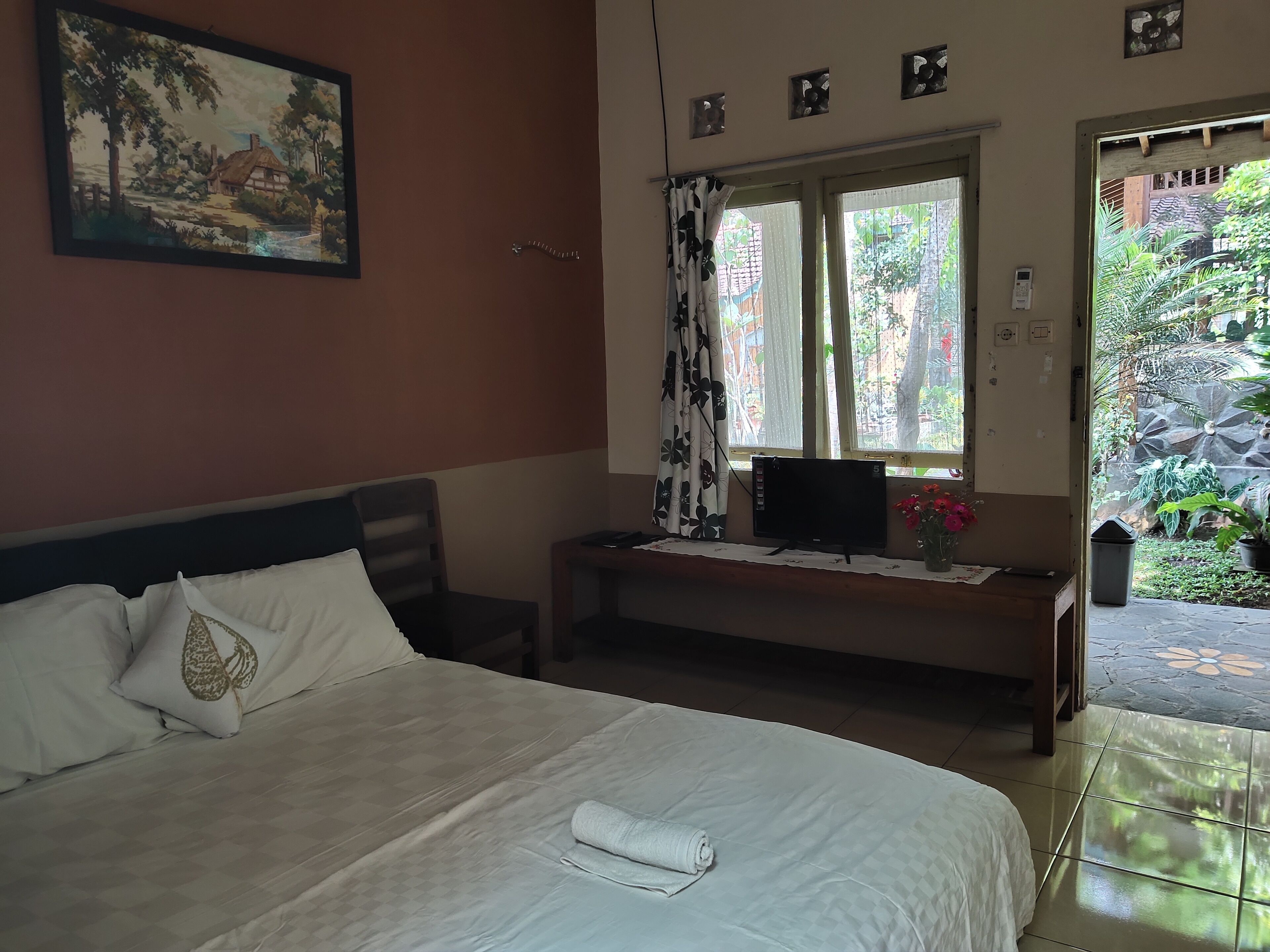 A hotel room with a bed, a desk with a TV, a window with curtains, and a painting on the wall.