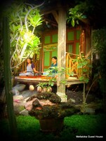 Una casa de madera tradicional con un porche, rodeada de abundante vegetación y un pequeño jardín.