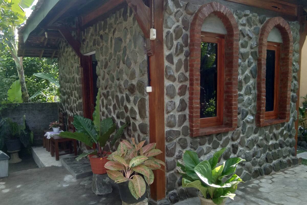 A stone building with arched windows and a covered patio area with potted plants.