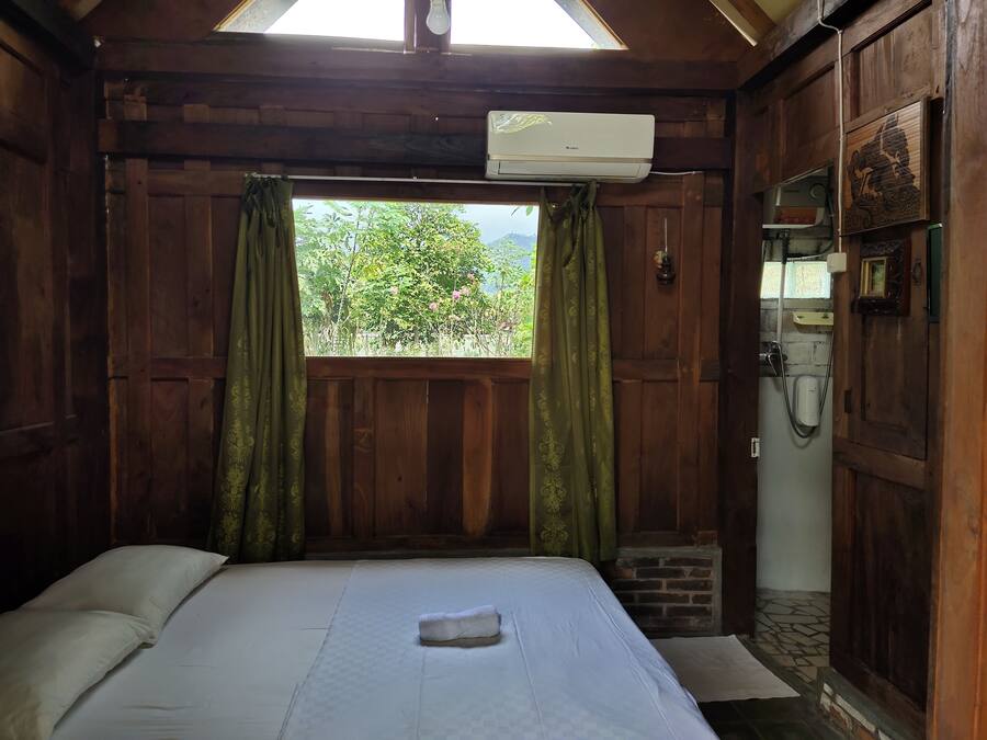 Una stanza con un letto, una finestra con tende, un condizionatore d'aria e una piccola struttura in mattoni.