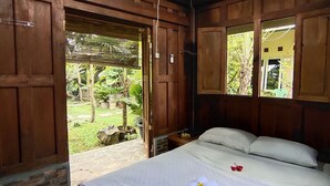 A wooden room with a bed, a window, and a door leading to an outdoor area. - Mettaloka Guest House and Art Space (Borobudur)