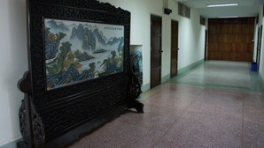 Un couloir orné d’une peinture chinoise traditionnelle au mur, avec une porte en bois au fond et un sol carrelé.