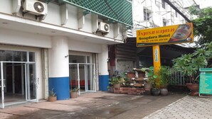 L’entrée d’un hôtel, avec une enseigne indiquant « Sengdara Hotel », des unités de climatisation et des plantes en pot.
